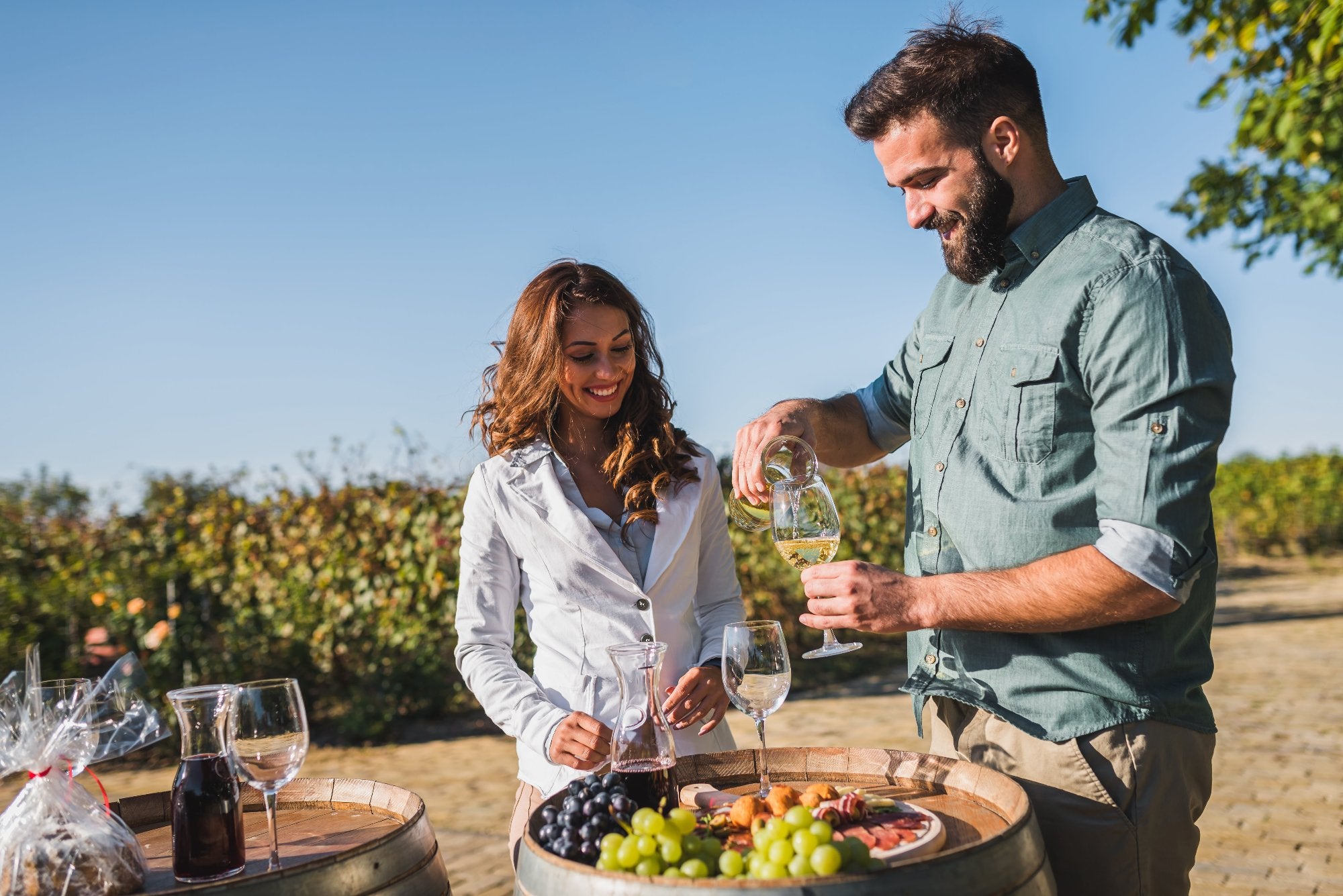 Two friends or couple serving white and red wine at a scenic vineyard in a sunny day