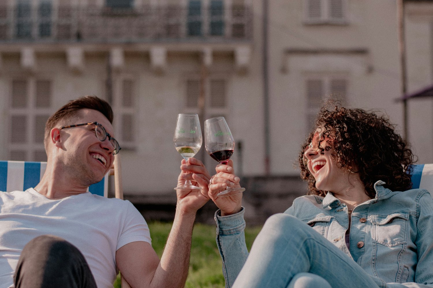 Two friends smiling sharing a red and white glass of wine in sunny setting