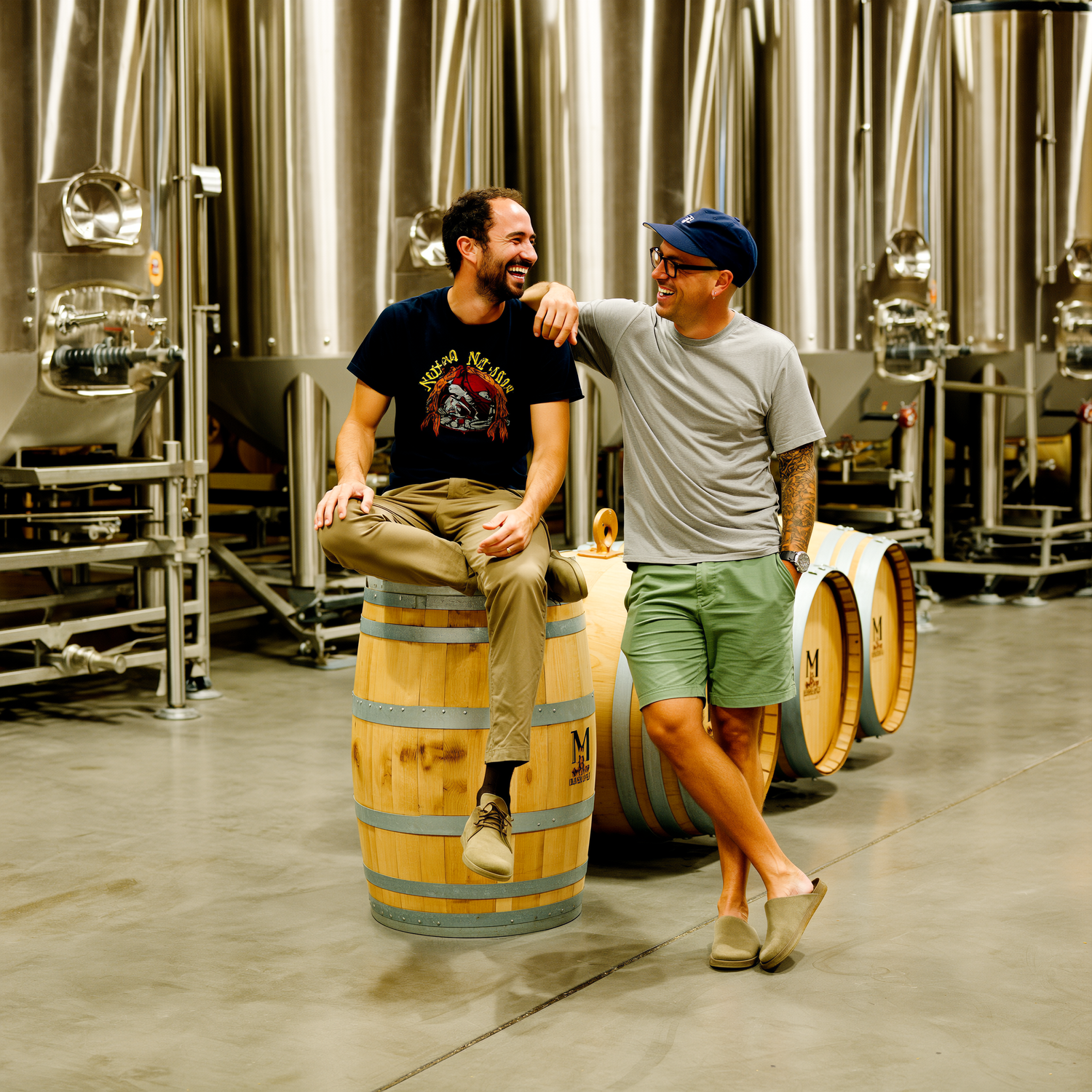 Two men sitting on barrels in a winery setting